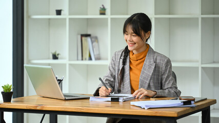 An attractive young businesswoman doing some paperwork and using laptop in a modern office