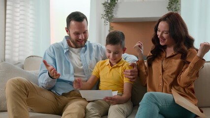 Excited Happy Caucasian family parents mother father child son receive paper notice letter at home on couch kid boy reading good news celebrating victory enjoying success great successful exam result