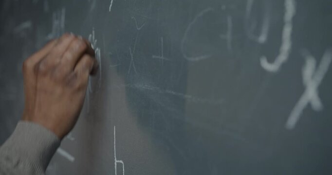Close-up of male hand writing formula on blackboard with chalk while scientist doing calculations and research. Science and mathematics concept.