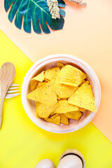 Corn chips on wooden plate isolated on orange and yellow background. Crispy snack dessert. Food Photography Concept