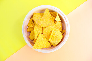 Corn chips on wooden plate isolated on orange and yellow background. Crispy snack dessert. Food Photography Concept