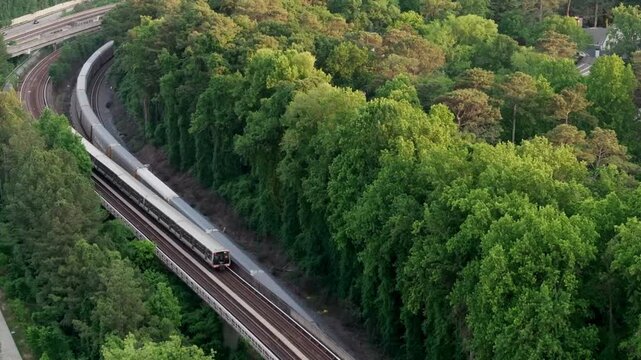 Drone shot of Atlanta metro rail and freight container shipping train crossing through nature forest trail, Georgia State Route 400, T Harvey Mathis Parkway