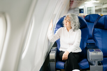 ￼Asian woman sitting in a seat in airplane and looking out the window going on a trip vacation travel concept