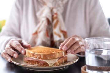 Unrecognizable elderly Caucasian woman ready to eat a french toast, lonely grandmother sitting outdoors at cafe table enjoys her sandwich