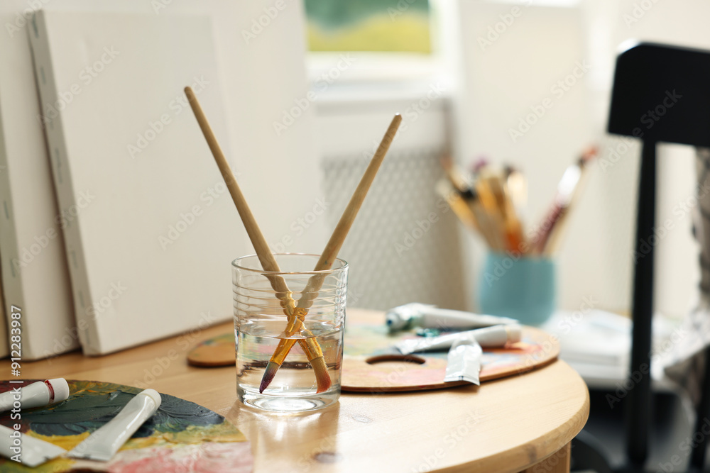 Poster Artist's palette, brushes in glass of water and paints on wooden table indoors