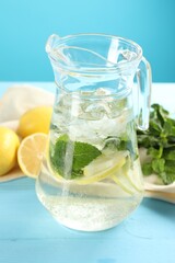 Refreshing lemonade with mint in jug on light blue wooden table