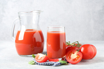 Tasty tomato juice with fresh vegetables and basil leaves on light grey table