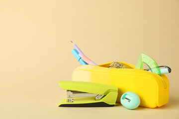 Green stapler and other stationery on beige background, space for text