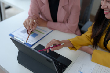 Two confident Asian businesswomen sitting at a table with laptops doing documents together and discussing reports. Project financial calculations brainstorming ideas.