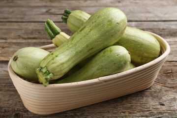 Raw green zucchinis in bowl on wooden table
