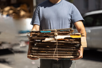 volunteer man holds tied paper pressed bales for further hazardous waste recycling front washed-out street. Separate garbage collection. Recycling and storage of waste for further disposal. banner