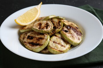 Tasty grilled zucchini slices with lemon on black table