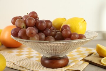 Fruit vase with grapes and lemon on wooden table in kitchen, closeup