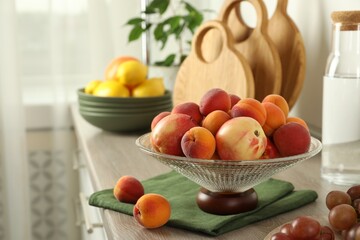 Glass vase with different fresh fruits on wooden countertop in kitchen. Space for text