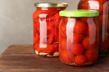 Different pickled vegetables in jars on wooden table, closeup