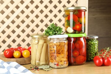 Different pickled products in jars, fresh tomatoes and spices on wooden table
