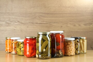 Different pickled products in jars on wooden table