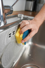 A close-up view of a man's hands using a sponge to clean the sink at home. A man engaged in household tasks, capturing the essence of everyday responsibilities and home maintenance