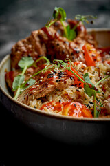 A bowl of beef teriyaki with rice, cherry tomatoes, and microgreens. The dish is served in a gray bowl on a dark background.