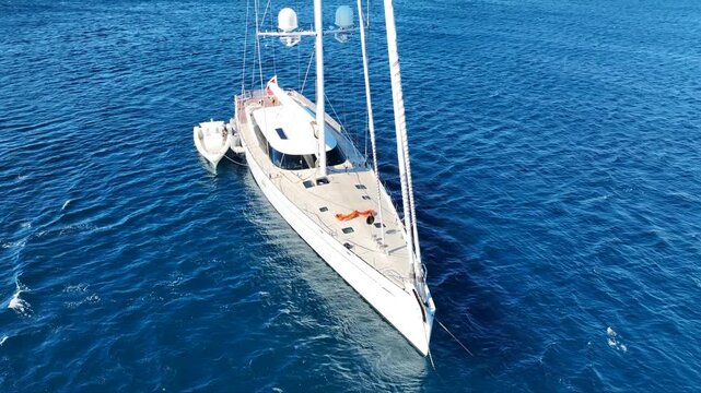 Aerial drone rotational video of beautiful sailboat with wooden deck anchored in deep blue sea near Mediterranean destination port