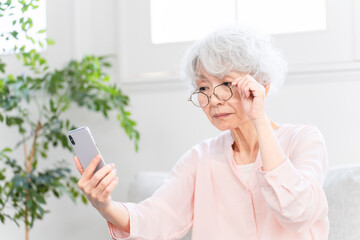 老眼でスマートフォンを見るのに苦労しているシニア女性