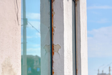 Cracked plaster and exposed insulation around window frame, exterior facade damage, weathering, need for repair. Foam insulation around the side jamb .
