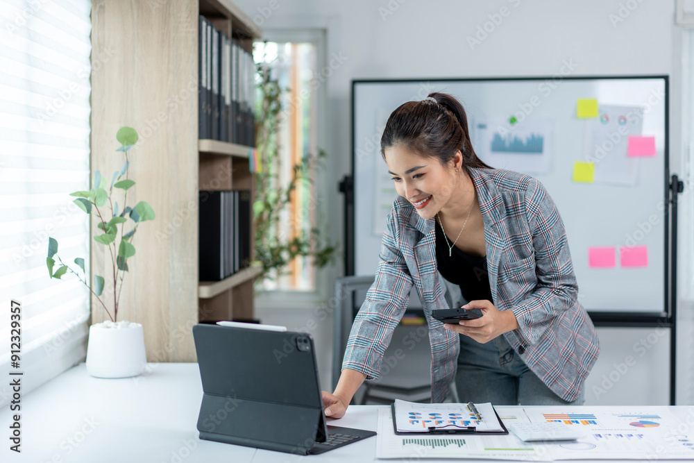 Wall mural A woman is sitting at a desk with a laptop and a cell phone