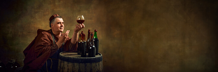 Deep history of monastic brewing. Man, medieval monk in robe raising glass filled with brown liquid, beer, ale, cognac against vintage background. Concept of comparison of eras, history, traditions