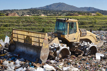 Heavy machinery shredding garbage in an open air landfill. Pollution