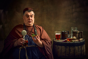 Medieval monk enjoying sandwich with fish, degustating ale, beer and cognac against vintage...