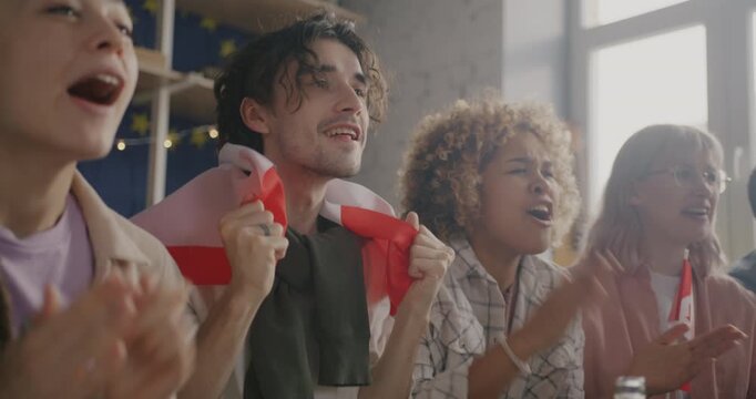 Slow motion of young people sports fans with Canadian flags watching competition on TV cheering having fun at home. Youth and hobby concept.