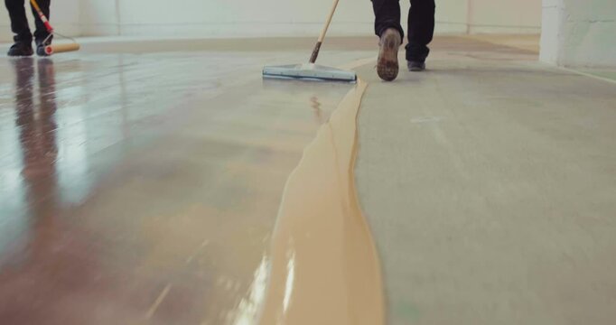 Workers applying a base coat of epoxy resin support using a floor squeegee on the existing concrete surface. Slow motion.