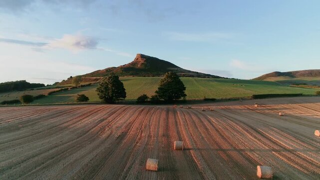 Harvest time at Aireyholme Farm in the shadow of Roseberry Topping, North York Moors National Park. Drone footage flying over a harvested field with hay bales and a closer view.