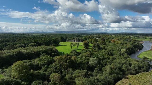 Castle Saunderson, County Cavan, Ireland, September 2022. Drone orbits clockwise around the old Gothic Revival Castle ruins with lawns surrounded by trees with the Finn River in the background.