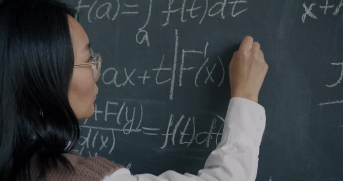 Intelligent Asian lady mathematician writing on chalkboard concentrated on science and maths. Academic education and master degree concept.