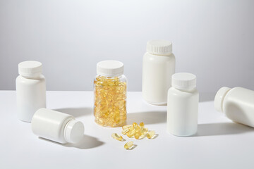 Transparent bottle filled with golden omega 3 capsules, displayed in the center of white countertop with some white unbranded bottle surround. High angle shot, blank space for designing