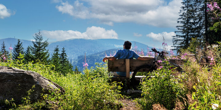 Radfahrer macht Pause auf einer Bank mit Blick auf den Feldberg im Schwarzwald