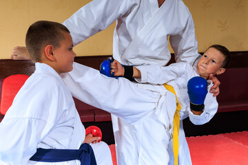 Athlete in blue pads throws a roundhouse kick at an athlete in red pads with the help of a trainer