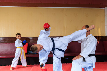 A boy athlete in red pads performs a roundhouse kick on the coach's hand