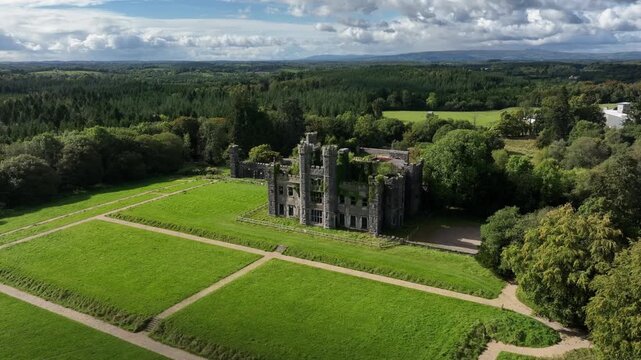 Castle Saunderson, County Cavan, Ireland, September 2022. Drone orbits counter clockwise and moves closer to ruined Stone Castle with lawns in front and forrest in background under a cloudy sky.