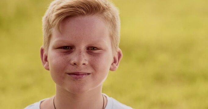 Close up portrait of young boy looking at camera. Non urban scene, windy day, yellow field, candid child enjoying beauty of nature, ukrainian teenager. High quality 4k footage