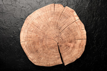 Round wooden board carved from tree trunk on black concrete background. Can be used like natural...