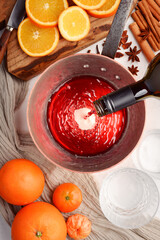 Red wine pouring into a copper pot from bottle. Making mulled wine in home kitchen. Slices of orange, cinnamon, star anise on table. Food photography