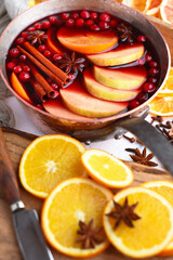 Copper pot full of red mulled wine with slices of orange, apple, cinnamon, star anise, rosemary and cranberries on wooden table. Food photography