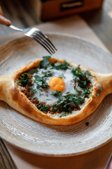 sweet girl in a blue dress is eating delicious khachapuri with juicy meat, fresh vegetables, fragrant herbs, and crispy dough on a beautiful white plate in a cozy nice restaurant