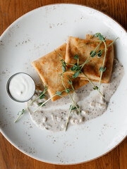 Delicious pancakes with fragrant herbs and sour cream-cream sauce on a beautiful white plate in a cozy nice restaurant