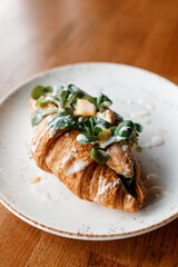 delicious croissant with juicy chicken, fragrant herbs, and creamy sauce on a beautiful white plate in a cozy nice restaurant