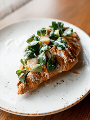delicious croissant with juicy chicken, fragrant herbs, and creamy sauce on a beautiful white plate in a cozy nice restaurant