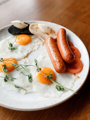 delicious English breakfast with juicy sausages, fresh vegetables, fragrant herbs, and scrambled eggs on a beautiful white plate in a cozy nice restaurant