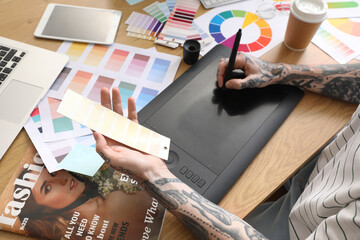 Tattooed graphic designer working with tablet and paint palette on table in office, closeup